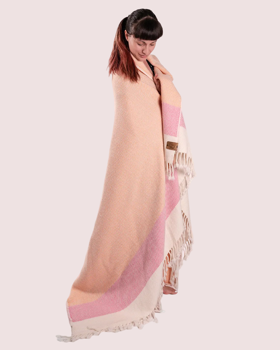 A person standing and wearing a peach-colored, pink, and orange striped blanket as a scarf.